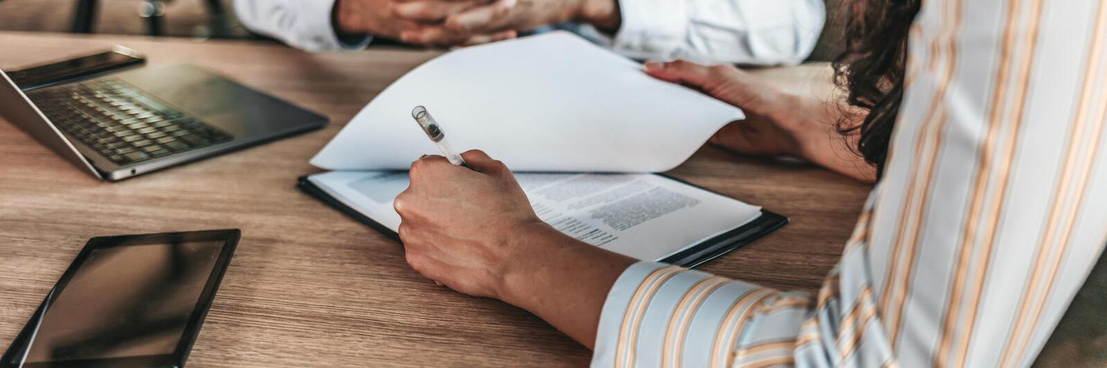 Gros plan d'une main féminine signant un document formel sur la table d'un bureau